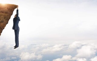 resilient person hanging from a cliff above blue clouds